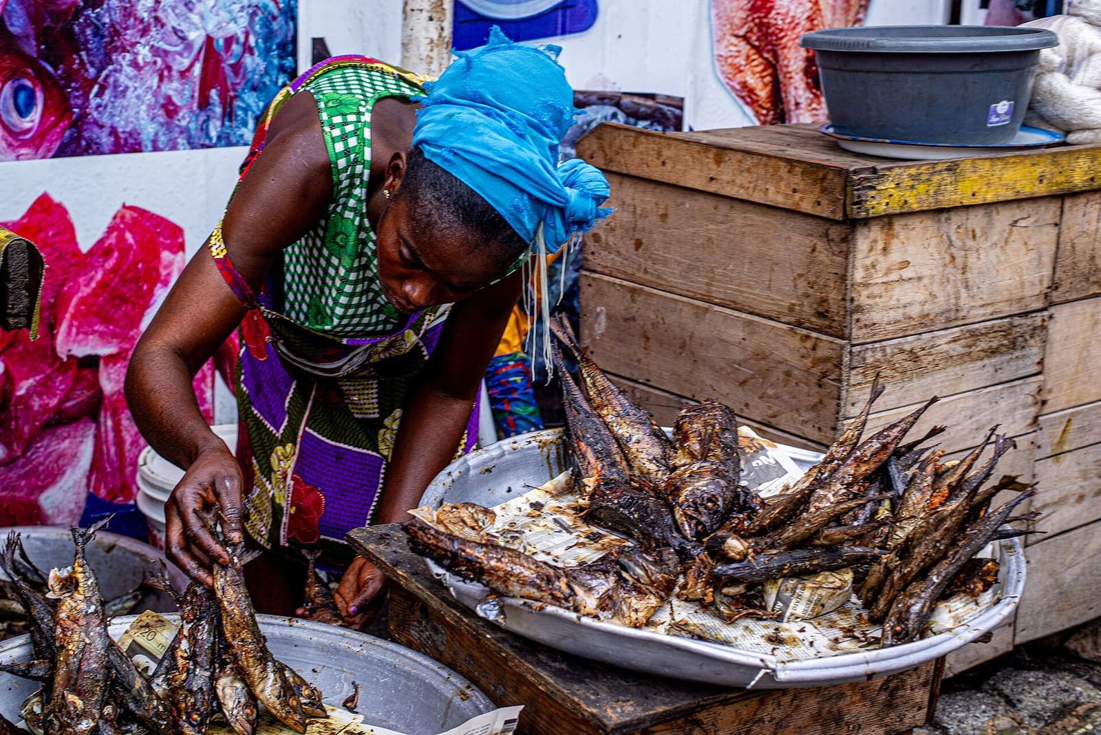 A fish seller arranges smoked fish in a basin at her market stall.